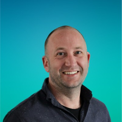 Portrait of Tim Drijvers smiling, wearing a dark shirt against a teal background